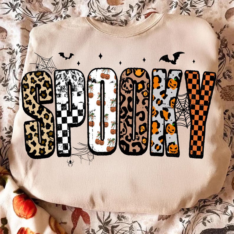 May include: Beige sweatshirt with the word "SPOOKY" in large, patterned letters. The letters feature leopard print, checkerboard, pumpkin, and spiderweb designs, with bat and star accents. A festive Halloween-themed garment.