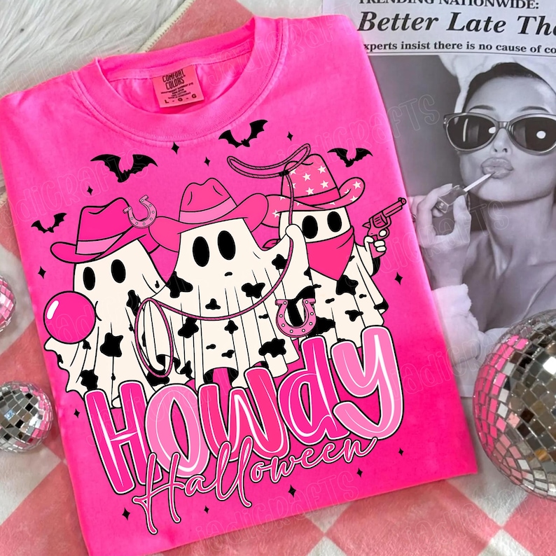 May include: A bright pink sweatshirt featuring a graphic of three ghost cowboys with cowboy hats, bandanas, and a lasso. The text "Howdy Halloween" is displayed in pink. Bats and horseshoes are also featured in the design.