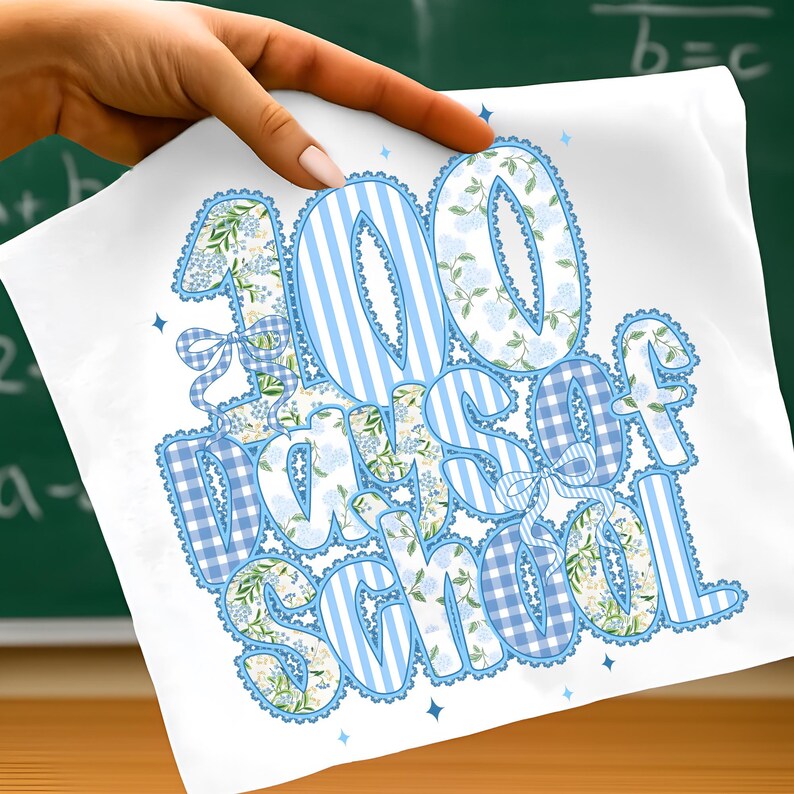 K&ouml;nnte beinhalten: Wei&szlig;er Stoff mit dem Text "100 Days of School" in Blau. Die Zahlen und Buchstaben haben Blumen-, Streifen- und Vichy-Muster. Eine Hand h&auml;lt den Stoff vor einer Tafel.