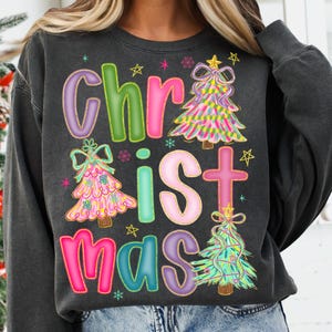 May include: Dark gray sweatshirt with the word "Christmas" in colorful, bubble letters. The design includes Christmas trees and stars in pink, green, and yellow. A festive holiday-themed top.