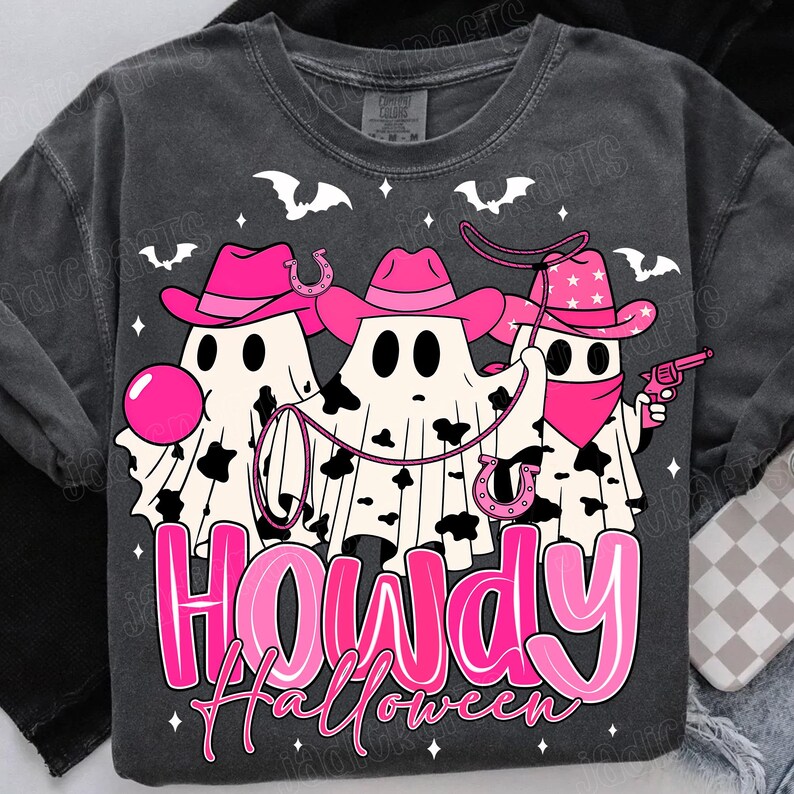 May include: Dark gray t-shirt featuring a Halloween-themed graphic. The design includes three ghost figures wearing pink cowboy hats and bandanas, with a lasso and a toy gun. The text "HOWDY Halloween" is displayed in pink.