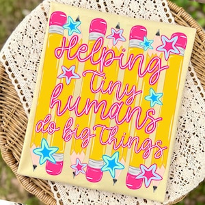 May include: A rectangular sign with a light yellow background featuring a repeating pattern of yellow pencils with pink erasers. The text "Helping tiny humans do big things" is written in a cursive pink font, accented by small blue and pink stars.