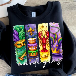 May include: Black sweatshirt with a colorful Mardi Gras design. The design features a mask, cake, crawfish, and a jester's hat. The text "Mardi Gras" is written in white letters at the bottom.