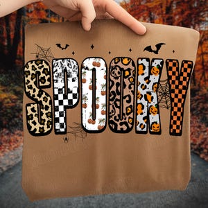 May include: A brown sweatshirt with the word "SPOOKY" in a variety of Halloween-themed patterns. The letters feature leopard print, checkerboard, pumpkins, and spiderwebs. Bats and stars are also included in the design.