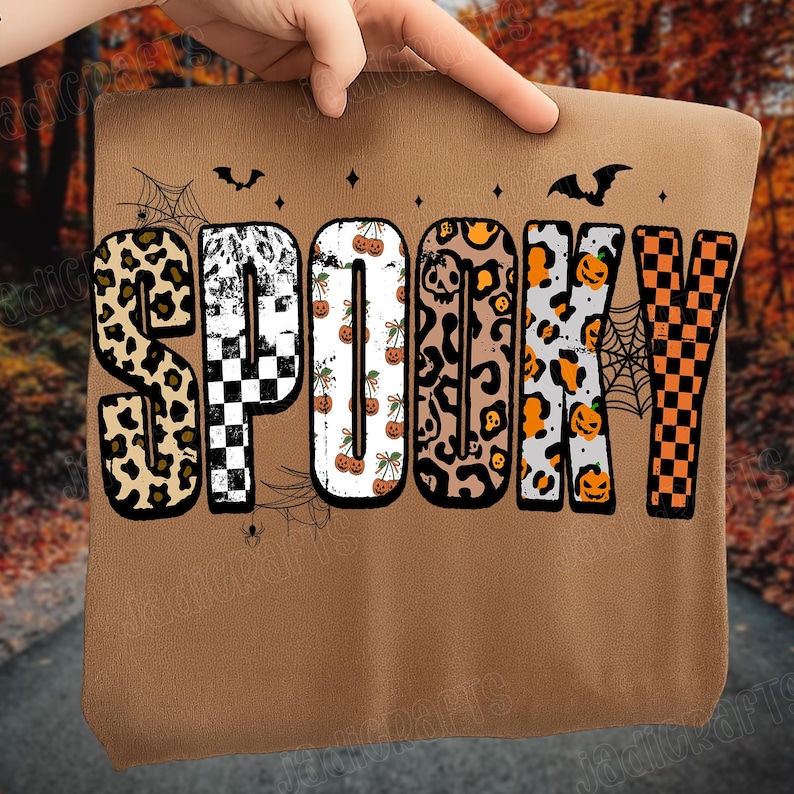 May include: A brown sweatshirt with the word "SPOOKY" in a variety of Halloween-themed patterns. The letters feature leopard print, checkerboard, pumpkins, and spiderwebs. Bats and stars are also included in the design.
