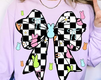 May include: A purple sweatshirt with a black and white checkered bow with pastel colored accents. The bow has a variety of small pastel colored designs including flowers, butterflies, and bunny shapes.