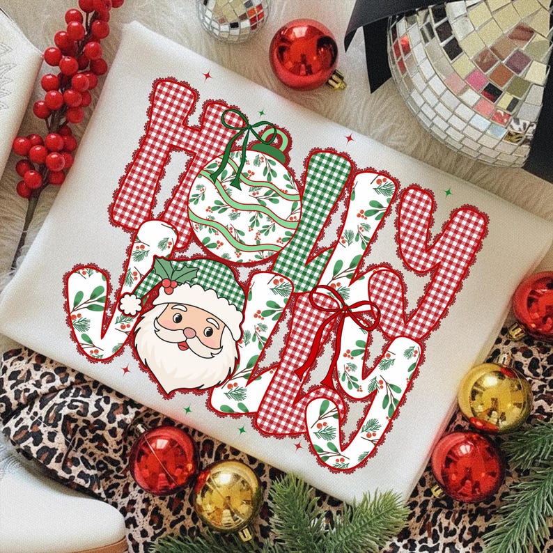 May include: A cream-colored sweatshirt with the word "JOY" in a festive design. The letters are a mix of red gingham, green plaid, and a floral pattern. A Santa Claus graphic and Christmas ornaments complete the holiday theme.