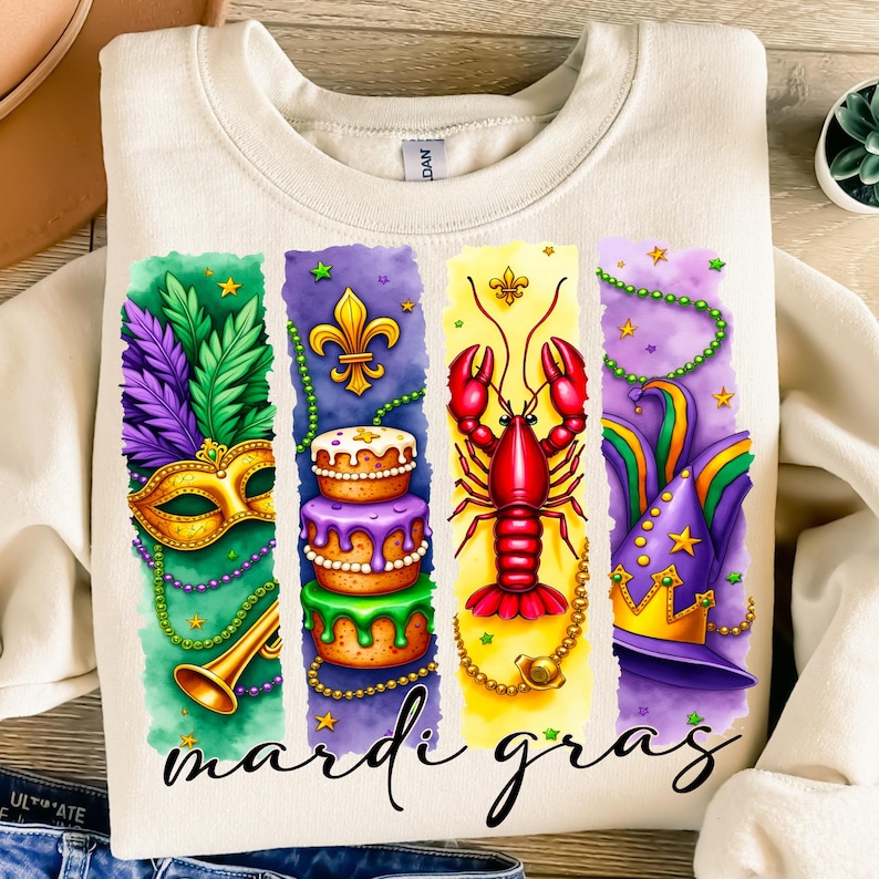 May include: A white sweatshirt with a colorful Mardi Gras design. The design features a purple, green, and gold mask, a cake with purple frosting, a red lobster, and a purple and gold hat. The text "Mardi Gras" is printed below the design.