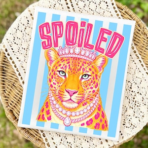 May include: A canvas print featuring a regal leopard wearing a crown and a pearl necklace. The word "SPOILED" is written in pink above the leopard's head. The background has blue and white vertical stripes.