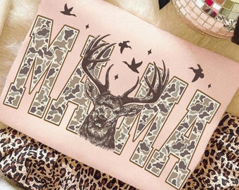 May include: A light pink sweatshirt with the word "MAMA" in a camouflage pattern. A deer head graphic is centered, with birds and stars. The sweatshirt is on a leopard print fabric.