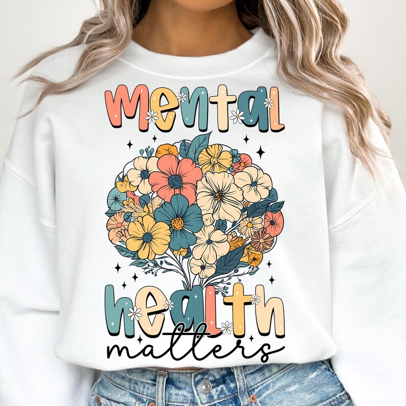 May include: White sweatshirt with a floral design and the text "Mental Health Matters." The floral arrangement features a variety of colorful flowers in shades of peach, blue, yellow, and orange. The text is in a retro font.