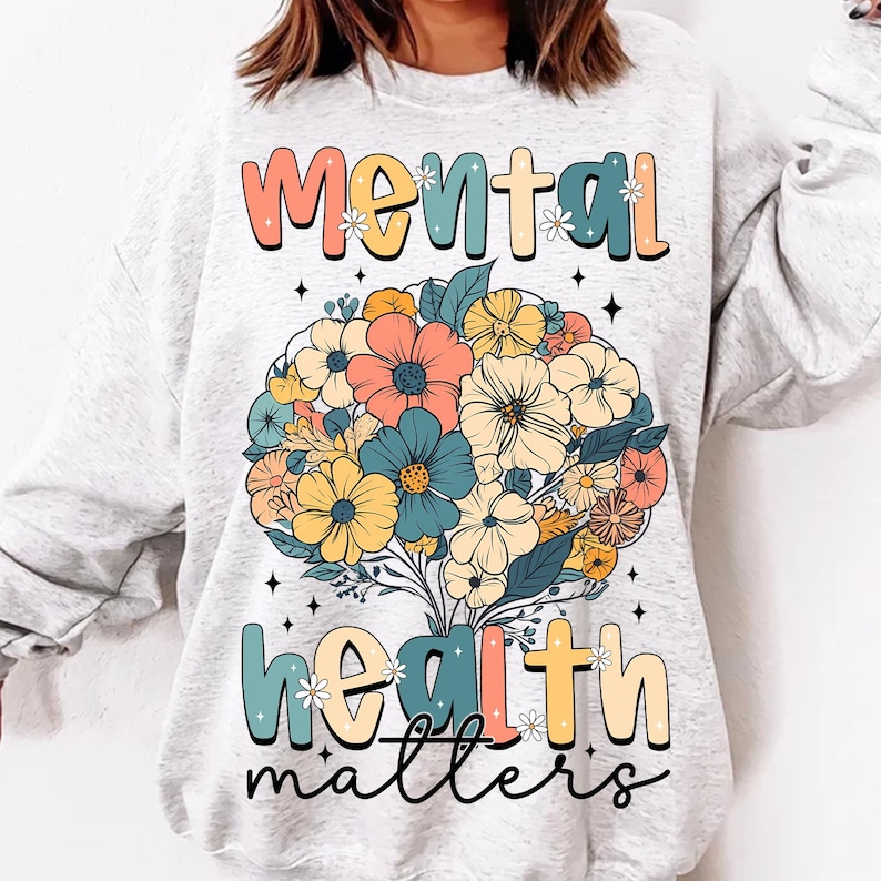 May include: A light gray sweatshirt with the words "MENTAL HEALTH matters" in colorful, retro-style lettering. A bouquet of flowers in shades of orange, blue, yellow, and pink is centered on the shirt.