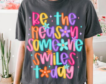 May include: A dark gray cropped t-shirt with the text "Be the reason someone smiles today" in colorful, outlined letters with flowers.