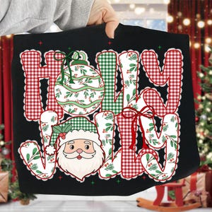 May include: Black t-shirt with the words "HOLY JOY" in a festive design. The letters are filled with red and white gingham, green plaid, and a floral pattern. A Santa Claus graphic and Christmas ornament are also featured.