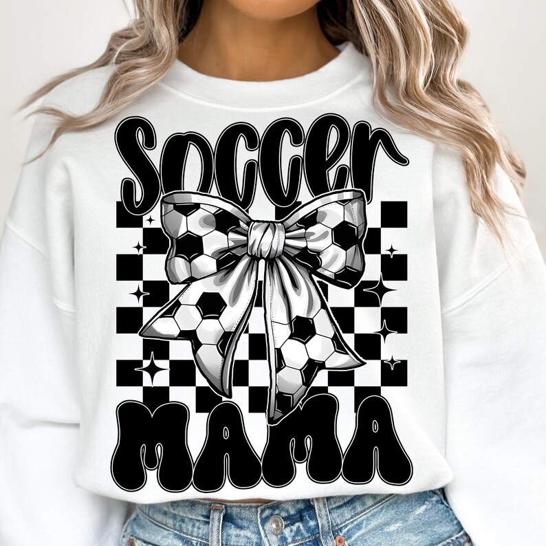May include: White sweatshirt with the words "Soccer Mama" in black, featuring a soccer ball bow design. The background has a black and white checkered pattern with star accents. A casual and sporty design.