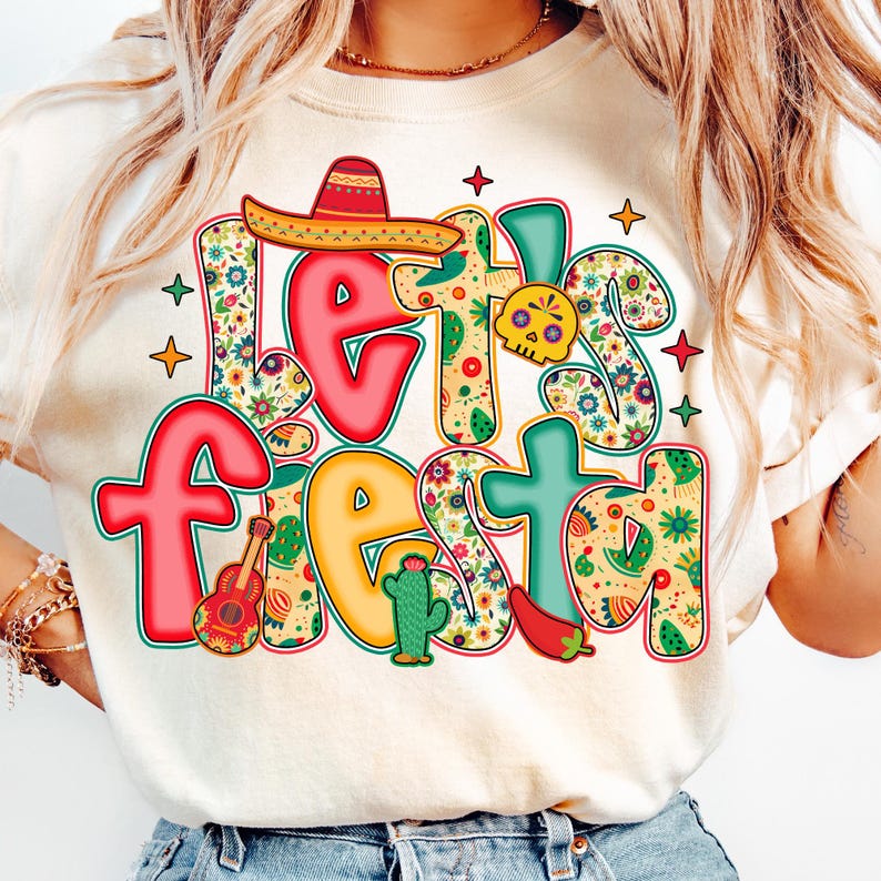 May include: Cream-colored t-shirt with the words "Let's Fiesta" in a colorful, festive design. The design includes a sombrero, guitar, cactus, skull, and chili pepper, all with floral patterns.