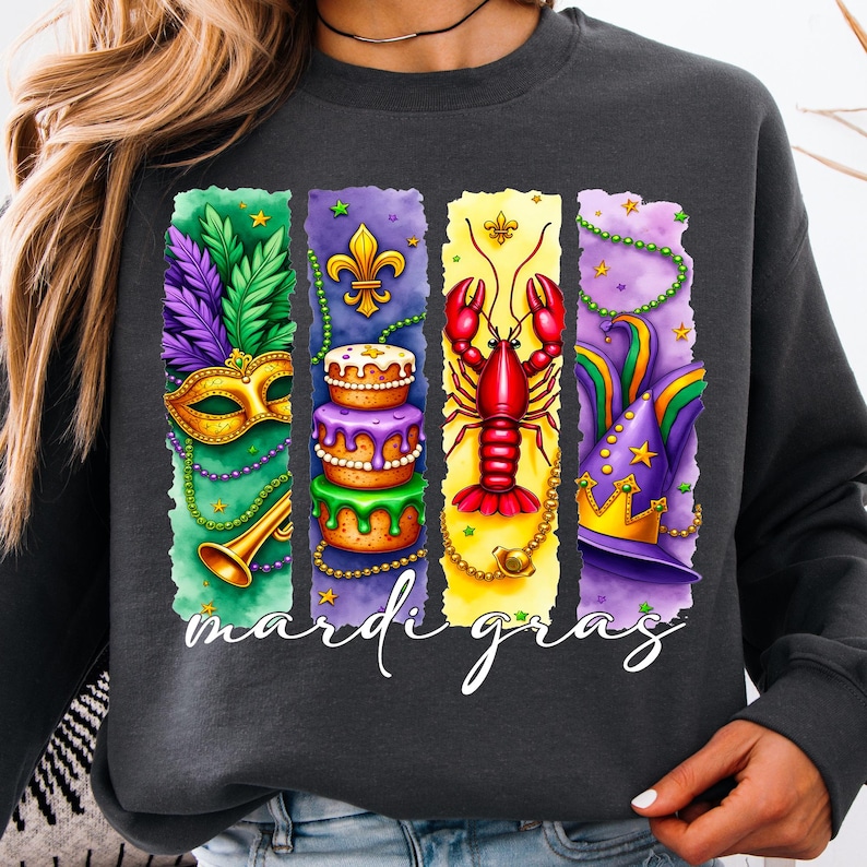 May include: A dark gray sweatshirt with a colorful Mardi Gras design. The design features a mask, a cake, a crawfish, and a hat with stars. The text "Mardi Gras" is printed below the design.