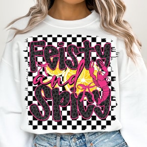 May include: White sweatshirt with a black and white checkered background. The text "Feisty and Spicy" is written in black with a leopard print pattern. A pink crawfish is on the right side of the text with yellow lemon slices behind it.