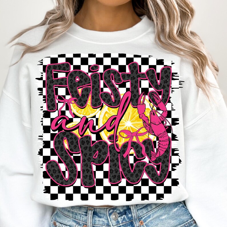 May include: White sweatshirt with a black and white checkered background. The text "Feisty and Spicy" is written in black with a leopard print pattern. A pink crawfish is on the right side of the text with yellow lemon slices behind it.