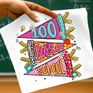 以下が含まれることがあります： 100日間の学校を祝うカラフルなデザインの白い布。デザインには、「100 Days of School」という言葉が鮮やかな色で書かれた3つのペナントバナーと、リンゴや定規などの学校をテーマにしたグラフィックが含まれています。