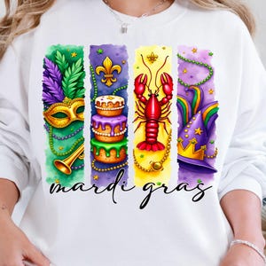 May include: White sweatshirt with a colorful Mardi Gras design. The design features a king cake, a crawfish, a mask, and a jester's hat. The text "Mardi Gras" is printed below the design.