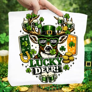 May include: White tote bag featuring a deer with antlers adorned with shamrocks and mugs of beer. The deer wears green sunglasses that read "Lucky Deer". The design includes a horseshoe, gold coins, and the text "Lucky Deer!"