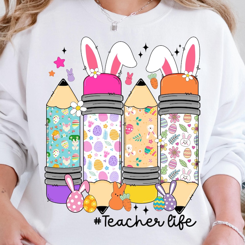 Op de afbeelding: Wit sweatshirt met een afbeelding van vier potloden versierd met paasmotieven en konijnenoren. De tekst "#Teacher life" is onder de potloden gedrukt.