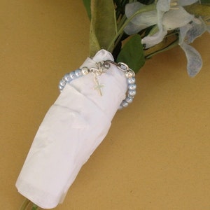 May include: A bouquet of light blue flowers wrapped in white tissue paper with a silver chain bracelet with a small silver cross charm.