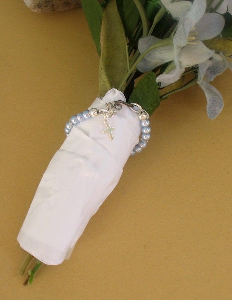 May include: A bouquet of light blue flowers wrapped in white tissue paper with a silver chain bracelet with a small silver cross charm.