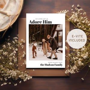 Può includere: Un biglietto di Natale con il testo "Oh Come Let Us Adore Him" e "Warm Wishes From the Hudson Family." Il biglietto mostra una famiglia che gioca sulla neve. Un adesivo circolare recita "E-VITE INCLUDED."
