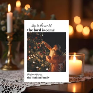 Könnte beinhalten: Eine Weihnachtskarte mit einem Foto eines geschmückten Weihnachtsbaums und zwei Personen. Die Karte trägt den Text "Joy to the world the lord is come" und "Christmas blessings, the Hudson Family."