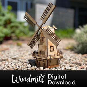 May include: A wooden windmill model with a brown and white color scheme. The windmill has a small house with windows and a roof. The model is sitting on a bed of small rocks.