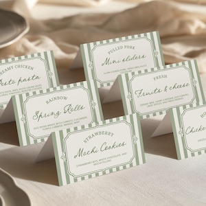 May include: A collection of folded table cards with menu items printed on them. The cards have a light green and white striped background with a decorative border. Menu items include "Creamy Chicken Pesto Pasta", "Pulled Pork Mini Sliders", and "Hot Honey Chicken & Waffles".