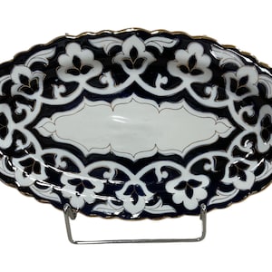 May include: Oval ceramic serving dish with a white center and a navy blue and white floral design around the edges. The dish has a gold trim and is displayed on a metal stand.