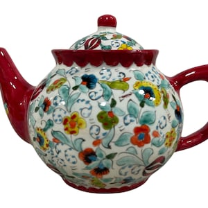 May include: A red and white ceramic teapot with a floral pattern. The teapot has a lid and a handle. The floral pattern is in shades of blue, green, yellow, and red.