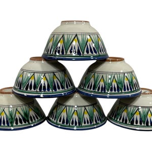 Puede incluir: Conjunto de seis cuencos de cerámica blanca con un patrón geométrico azul, verde y amarillo. Los cuencos están apilados en forma de pirámide.