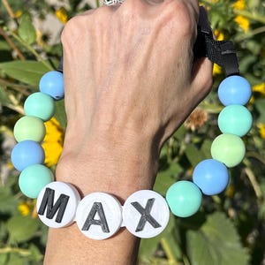 Op de afbeelding: Een blauwe en groene siliconen kralen armband met een witte kraal waarop "MAX" in zwarte letters staat.
