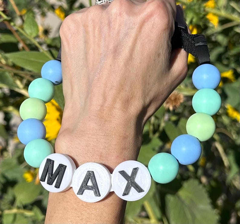 Op de afbeelding: Een blauwe en groene siliconen kralen armband met een witte kraal waarop "MAX" in zwarte letters staat.