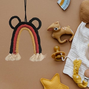 May include: A colorful rainbow macrame wall hanging with black, red, and yellow yarn. The rainbow has two small black ears at the top and is hanging from a string.