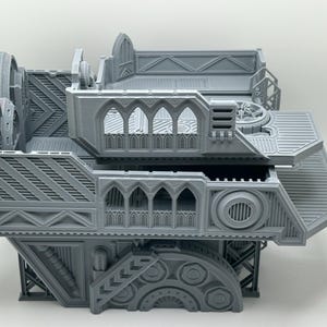 May include: A gray 3D printed model of a futuristic building with multiple levels and intricate details. The building has a gothic-inspired design with arched windows and a detailed facade.