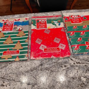Peut inclure: Trois paquets de papier cadeau sur le thème de Noël. Chaque paquet contient 12 feuilles, mesurant 76 x 102 cm. Les motifs comprennent des sapins de Noël, des traîneaux et des notes de musique. Les paquets sont étiquetés "100 Sq. Ft. Total 8 Assorted Designs."