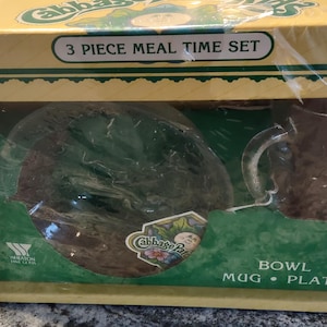 May include: A 3-piece Cabbage Patch Kids mealtime set in a brown box with a green and yellow design. The set includes a bowl, mug, and plate.