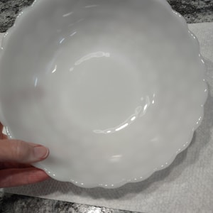 May include: A white, scalloped-edge bowl. The bowl is round with a smooth, glossy surface. The rim of the bowl has a decorative, wavy edge. The bowl is sitting on a white surface.