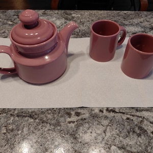 Puede incluir: Un juego de tres tazas de cerámica con un esmalte moteado de color crema. Cada taza presenta un diseño pintado a mano diferente: una hoja azul y verde, una flor amarilla y una baya roja. Las tazas tienen un diseño simple y moderno.