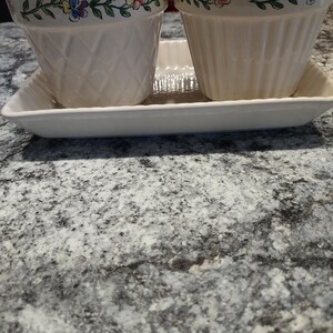 May include: Two white ceramic flower pots with a floral design around the top edge. The pots are sitting on a white ceramic tray.