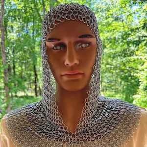 May include: A silver chainmail coif and gorget, designed to protect the head and neck. The coif covers the head and shoulders, with a detailed pattern of interlocking metal rings. The gorget is worn over a tan garment with a black emblem.