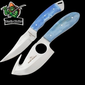 May include: Two stainless steel knives with light blue and white handles. One knife has a curved blade with a hook, and the other has a pointed blade. The handles have white rivets. The logo "Turtle Blades" is in the upper left corner.