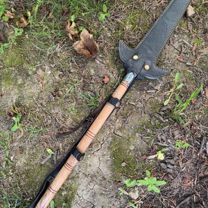 Pu&ograve; includere: Un'asta fatta a mano con una copertura della lama in pelle nera e un'asta di legno. La punta dell'asta &egrave; in pelle nera con cuciture gialle e rivetti in ottone. L'asta &egrave; in legno marrone chiaro con fasce metalliche e un cinturino in pelle.