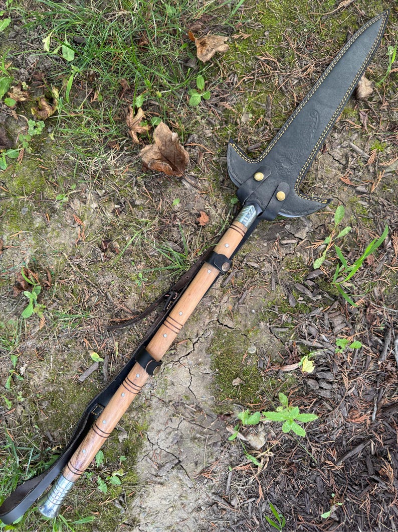 Pu&ograve; includere: Un'asta fatta a mano con una copertura della lama in pelle nera e un'asta di legno. La punta dell'asta &egrave; in pelle nera con cuciture gialle e rivetti in ottone. L'asta &egrave; in legno marrone chiaro con fasce metalliche e un cinturino in pelle.