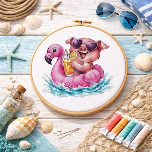 Puede incluir: Un bastidor de bordado de punto de cruz con un cerdo con gafas de sol en forma de corazón flotando en un flotador de flamenco rosa. El cerdo sostiene una bebida. El fondo incluye conchas marinas, gafas de sol e hilo.